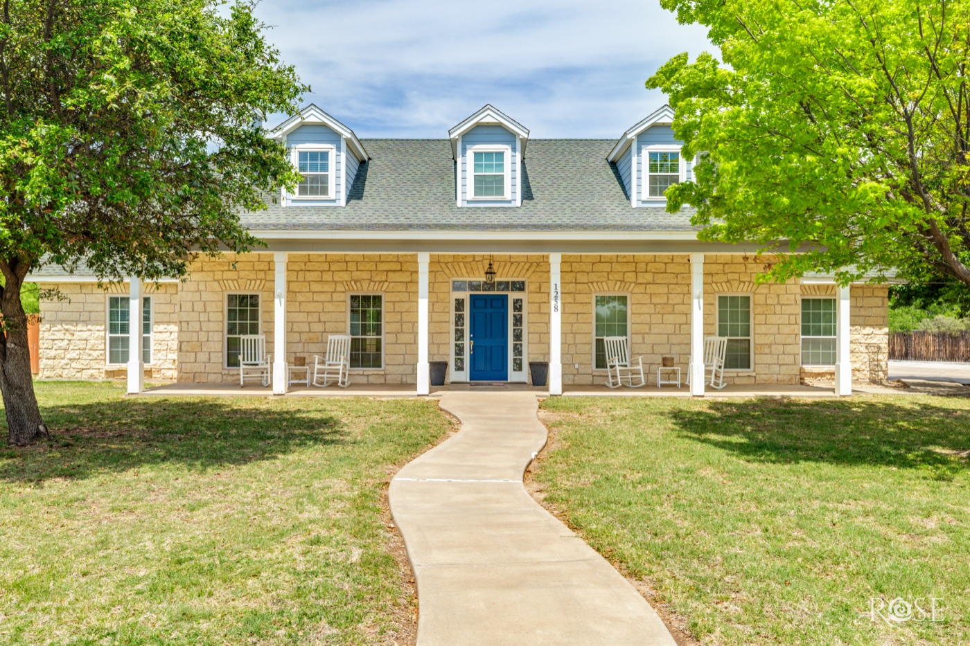Limestone home with dormer windows, a covered porch with rocking chairs, and a blue front door