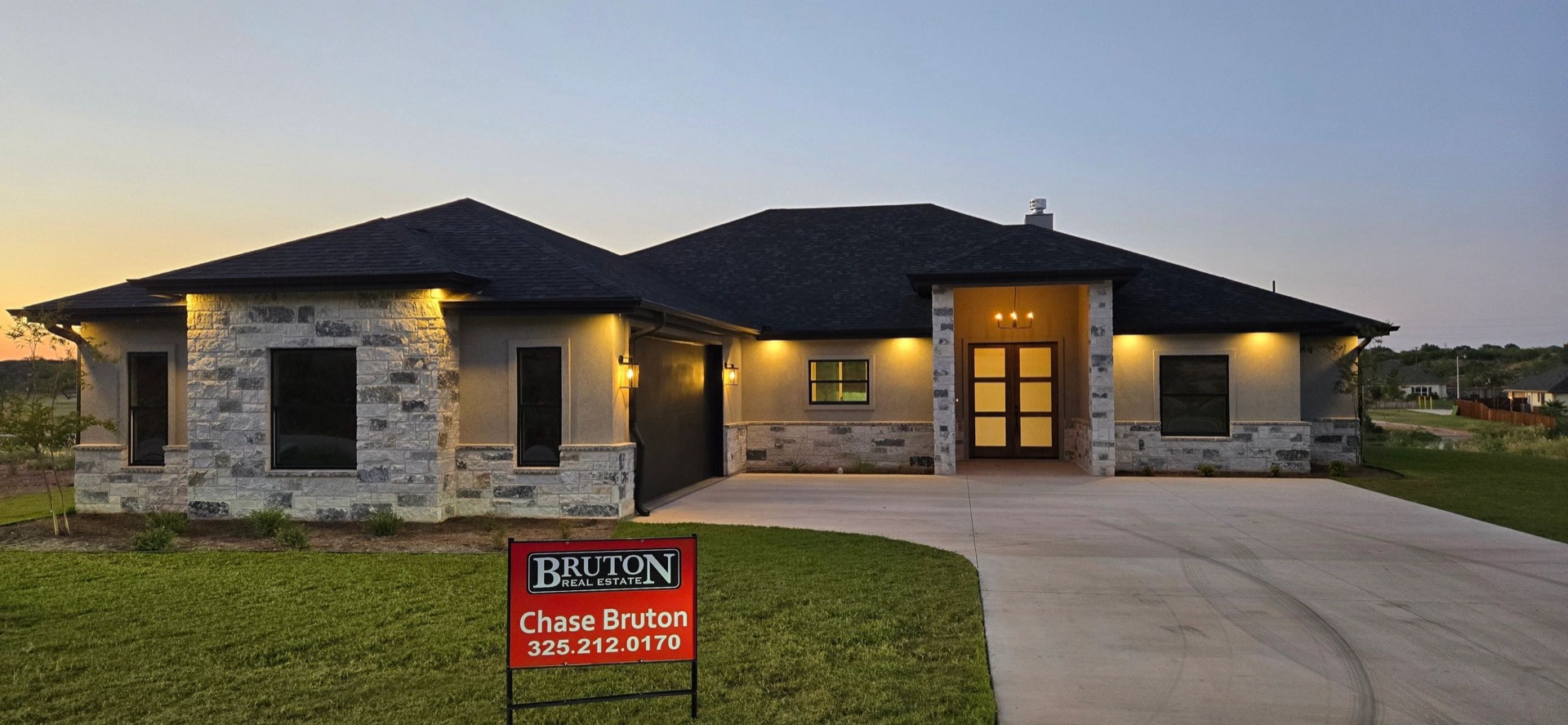 Stone and stucco home at dusk in San Angelo with a Bruton Real Estate sign in the yard